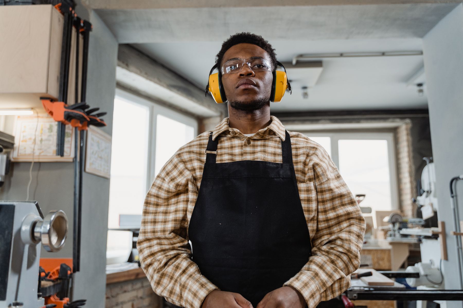 A carpenter wearing ear protection and an apron in a woodworking workshop